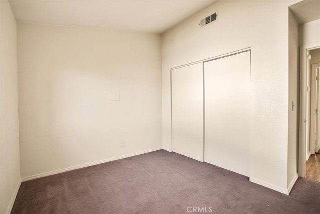 unfurnished bedroom featuring visible vents, baseboards, dark carpet, and a closet