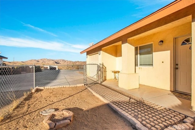 view of property exterior with fence, stucco siding, a gate, a patio area, and a mountain view