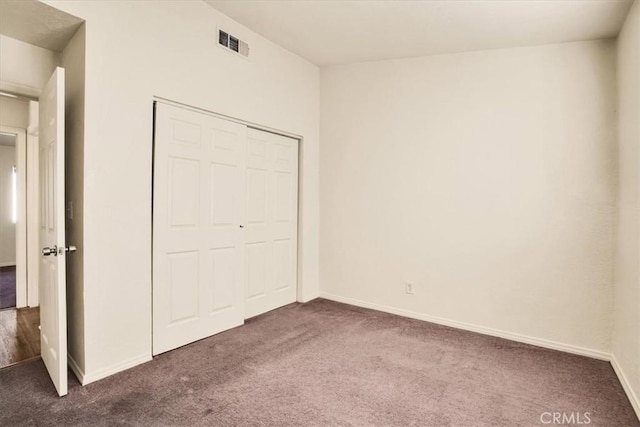 unfurnished bedroom featuring dark carpet, baseboards, visible vents, and a closet