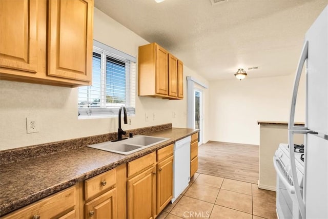 kitchen featuring visible vents, dark countertops, a sink, light tile patterned floors, and white appliances