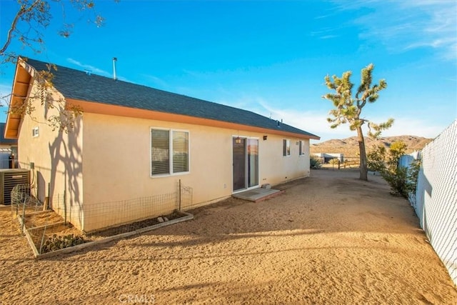 rear view of property featuring central AC unit, stucco siding, a shingled roof, and fence