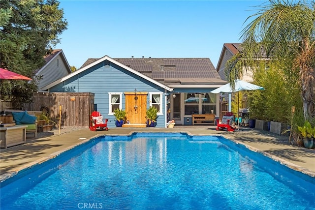 back of house with fence, a patio, an outdoor living space, a fenced in pool, and solar panels