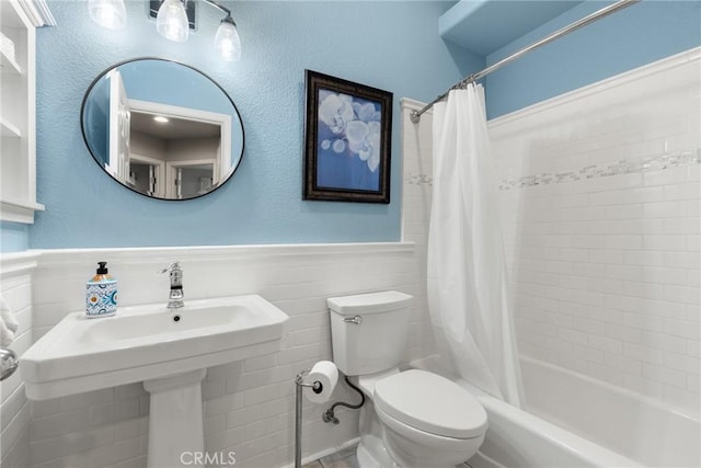 bathroom featuring toilet, wainscoting, a sink, and shower / bath combo with shower curtain