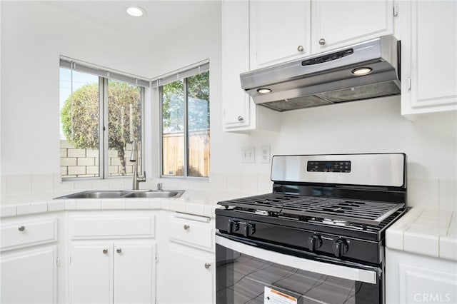 kitchen with stainless steel gas range oven, under cabinet range hood, tile countertops, and white cabinetry