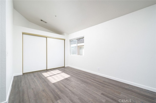 unfurnished bedroom featuring a closet, vaulted ceiling, wood finished floors, and visible vents