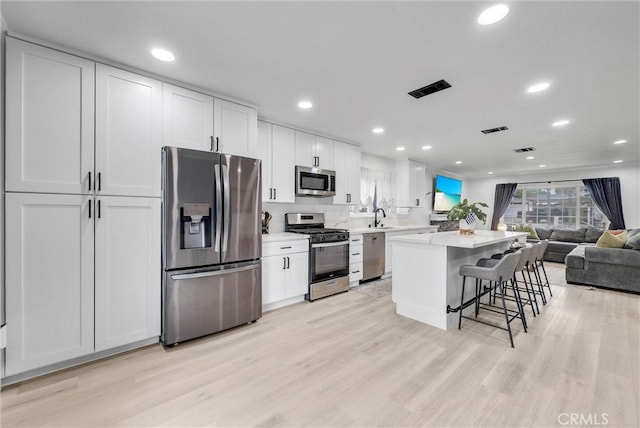 kitchen featuring stainless steel appliances, a sink, a center island, a breakfast bar, and light wood-style floors
