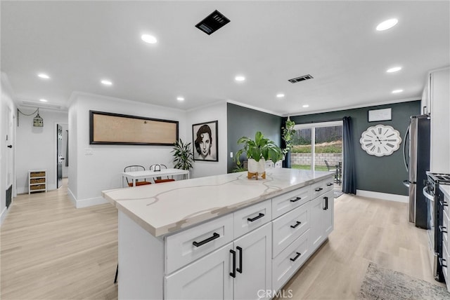 kitchen featuring a kitchen island, ornamental molding, baseboards, light stone counters, and white cabinets