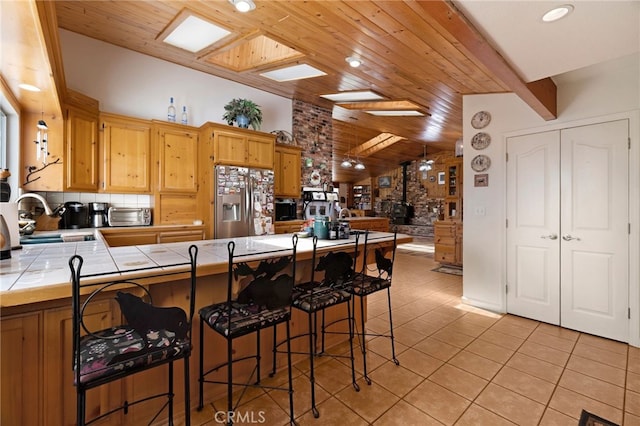 kitchen featuring wood ceiling, a sink, stainless steel fridge, tile counters, and light tile patterned flooring