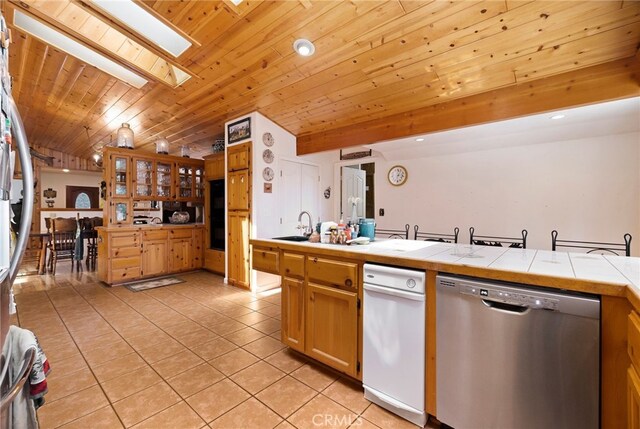 kitchen featuring light tile patterned flooring, dishwasher, tile countertops, wooden ceiling, and a skylight