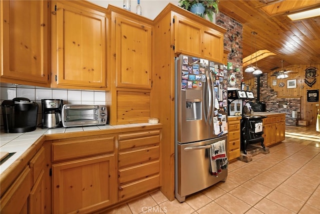 kitchen with a wood stove, tile counters, wooden ceiling, light tile patterned floors, and stainless steel refrigerator with ice dispenser