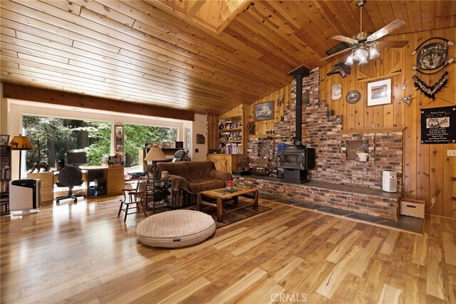 living area featuring wood-type flooring, a wood stove, wood ceiling, a ceiling fan, and vaulted ceiling