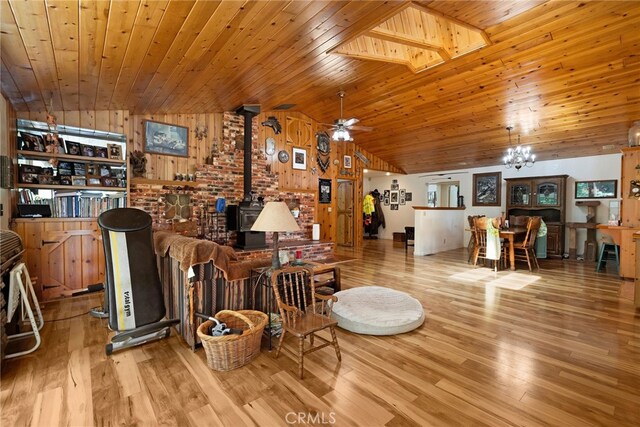 living room with a wood stove, lofted ceiling, wood finished floors, and ceiling fan with notable chandelier
