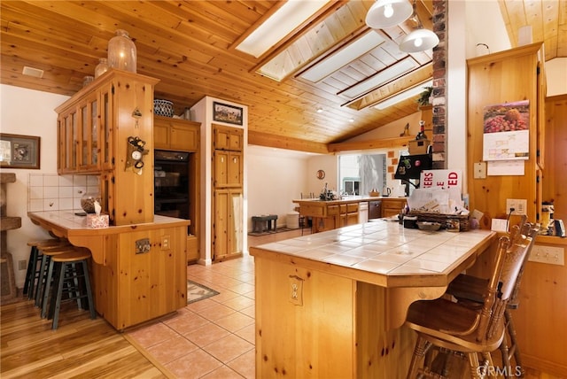 kitchen featuring wood ceiling, a breakfast bar area, a peninsula, lofted ceiling, and tile counters