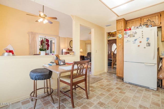 kitchen with stone finish floor, ceiling fan, brown cabinetry, visible vents, and freestanding refrigerator