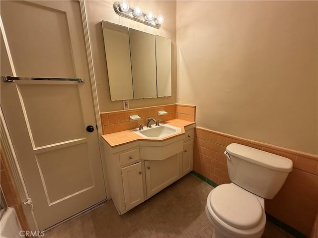 bathroom with vanity, toilet, tile walls, and a wainscoted wall