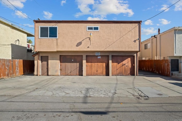 rear view of house featuring an attached garage, fence, driveway, and stucco siding