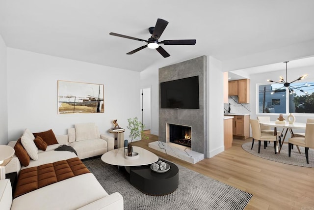 living area with light wood-style flooring, ceiling fan with notable chandelier, vaulted ceiling, and a premium fireplace