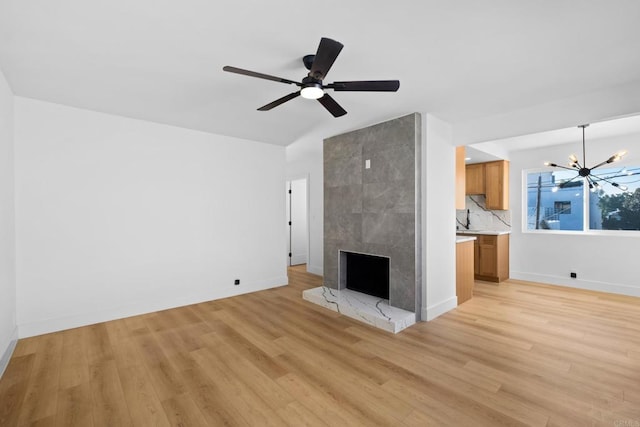 unfurnished living room with lofted ceiling, light wood-style floors, baseboards, a tile fireplace, and ceiling fan with notable chandelier