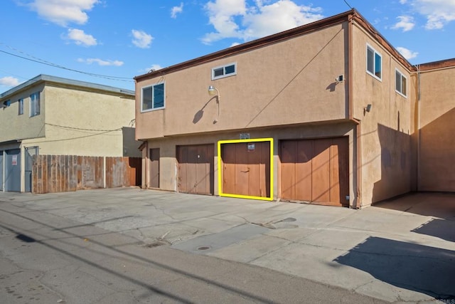 back of property with a garage, stucco siding, driveway, and fence