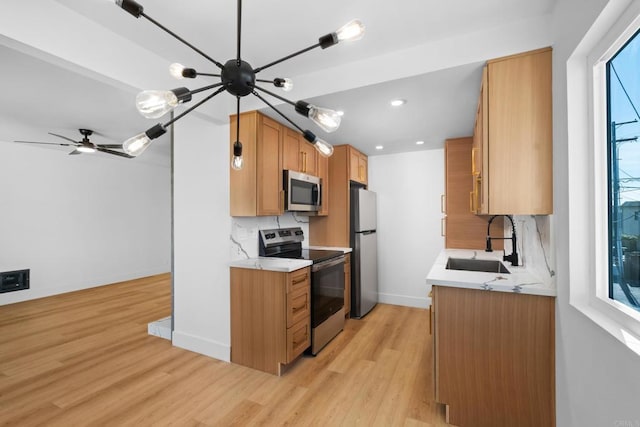 kitchen featuring tasteful backsplash, a sink, baseboards, light wood finished floors, and stainless steel appliances