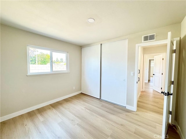 unfurnished bedroom featuring visible vents, light wood finished floors, baseboards, and a closet