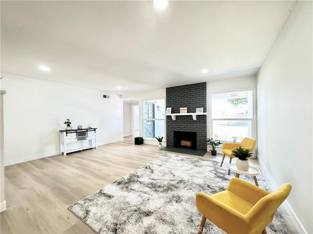 living area featuring light wood finished floors, a brick fireplace, and a healthy amount of sunlight