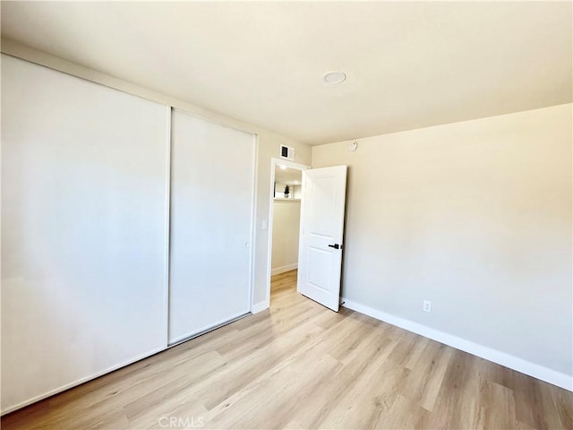 unfurnished bedroom with baseboards, visible vents, wood finished floors, and a closet