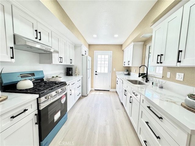 kitchen with a sink, stainless steel gas stove, freestanding refrigerator, white cabinetry, and under cabinet range hood