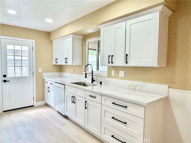 kitchen featuring light wood-type flooring, dishwasher, a sink, light stone counters, and white cabinetry
