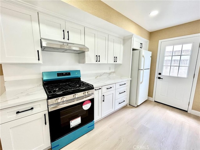 kitchen with under cabinet range hood, white cabinets, stainless steel range with gas cooktop, and freestanding refrigerator