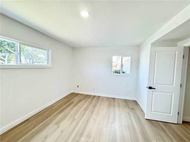 spare room featuring baseboards, light wood-style flooring, and a healthy amount of sunlight