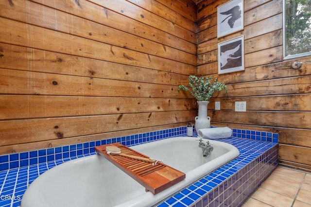 bathroom with tile patterned flooring, tiled tub, and wooden walls