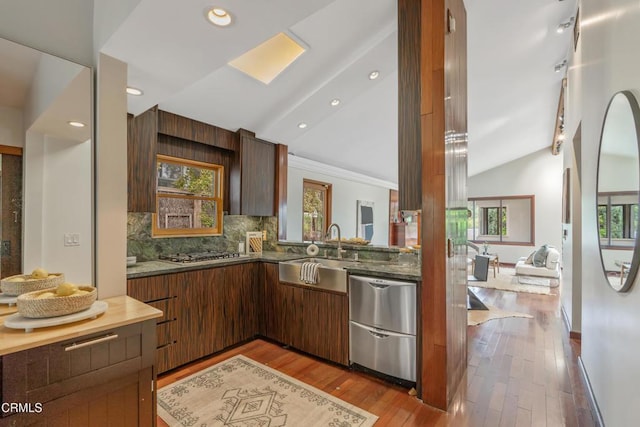 kitchen with appliances with stainless steel finishes, a sink, wood finished floors, backsplash, and vaulted ceiling