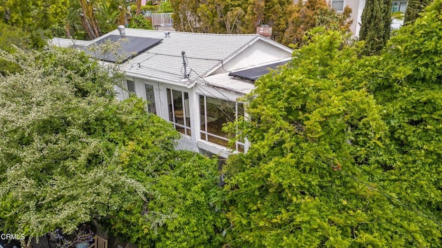 view of side of home with a chimney, a sunroom, solar panels, and metal roof