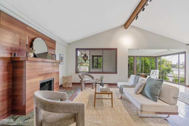 living room featuring track lighting, wood finished floors, baseboards, vaulted ceiling with beams, and a tiled fireplace