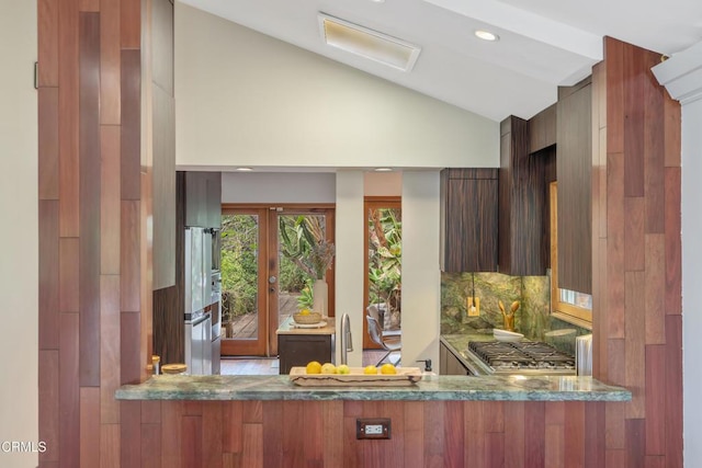 kitchen featuring backsplash, modern cabinets, stove, lofted ceiling, and stone counters