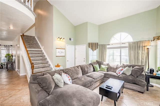 living room with visible vents, light tile patterned floors, high vaulted ceiling, baseboards, and stairs
