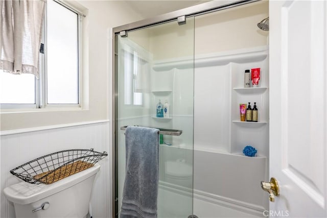 bathroom featuring toilet, a shower stall, and a wainscoted wall