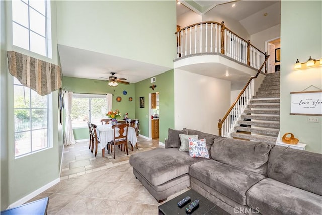 living area with high vaulted ceiling, ceiling fan, baseboards, and stairway