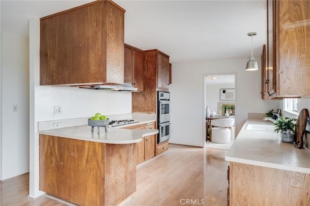 kitchen featuring light wood-style floors, a sink, stainless steel double oven, and light countertops