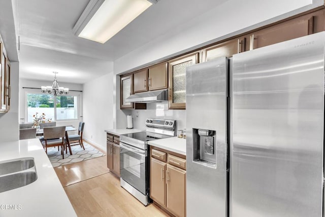 kitchen featuring an inviting chandelier, light countertops, stainless steel appliances, and under cabinet range hood