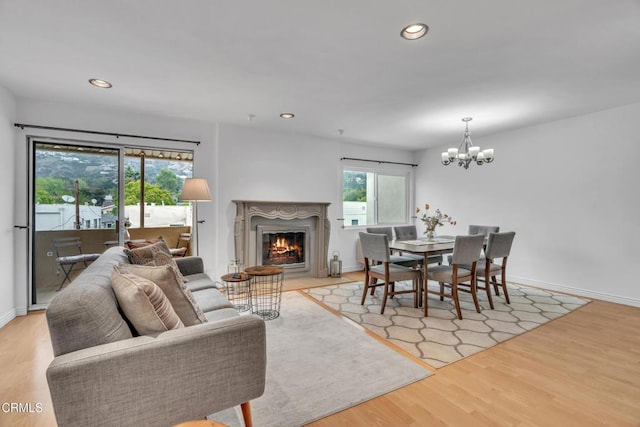 living area with a glass covered fireplace, light wood-style floors, recessed lighting, and a chandelier