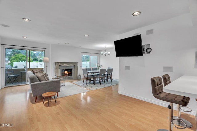 living room featuring baseboards, recessed lighting, light wood-style flooring, and a warm lit fireplace