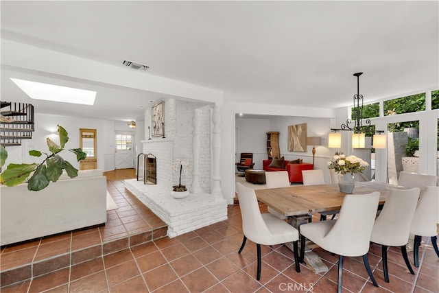 tiled dining area with visible vents, a brick fireplace, and a skylight
