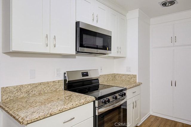 kitchen with visible vents, wood finished floors, light stone countertops, white cabinets, and stainless steel appliances
