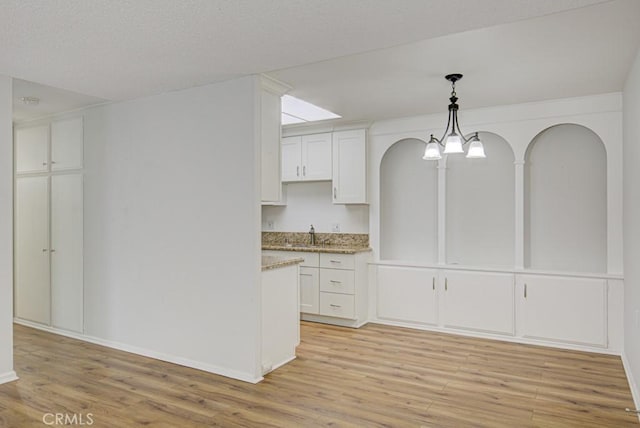 kitchen featuring light stone counters, arched walkways, white cabinetry, decorative light fixtures, and light wood-type flooring