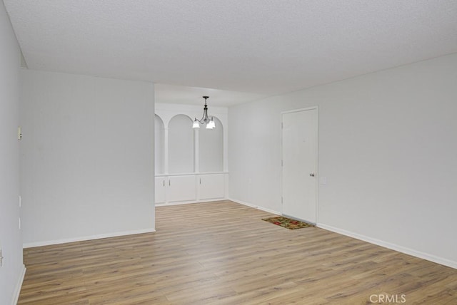 empty room with baseboards, a chandelier, and light wood-style floors
