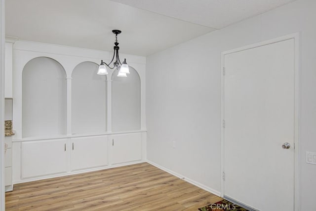 unfurnished dining area with arched walkways and light wood-style flooring