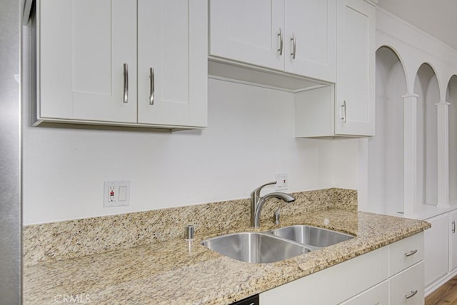 kitchen with a sink, white cabinetry, and light stone countertops