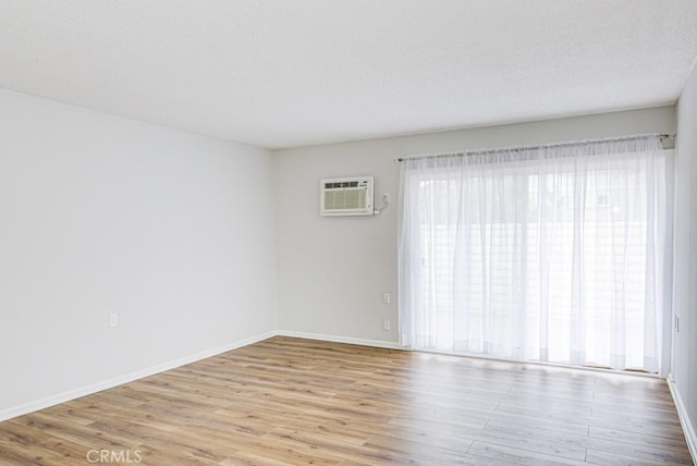 empty room with a textured ceiling, baseboards, an AC wall unit, and wood finished floors